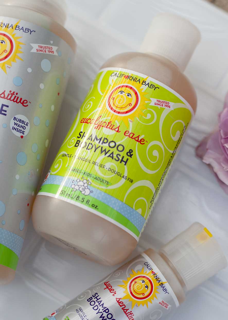 Bottle of California Baby - Eucalyptus Ease™ Shampoo & Bodywash with bright green and yellow packaging, surrounded by other baby care products on a soft white surface.