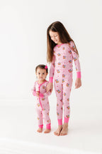 Two children wearing pink pajamas with cartoon characters on a white background
