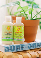 California Baby - Eucalyptus Ease™ Shampoo & Bodywash bottle displayed next to a tea tree & lavender hair conditioner on a book with a potted green plant in the background, styled for a cozy children’s boutique setting.