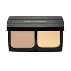 Open compact of Merle Norman Cosmetics - Expert Finish Makeup Broad Spectrum SPF 25 featuring beige pressed powder and light sponge applicator in sleek black case.