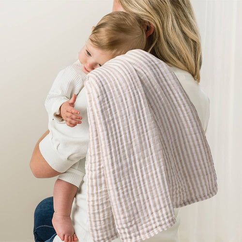 A mother holding her baby over her shoulder with a soft, textured burp cloth featuring a sage mudcloth pattern, emphasizing the Itzy Ritzy - Breastfeeding Boss™: Sage Mudcloth as a cozy mom life essential.