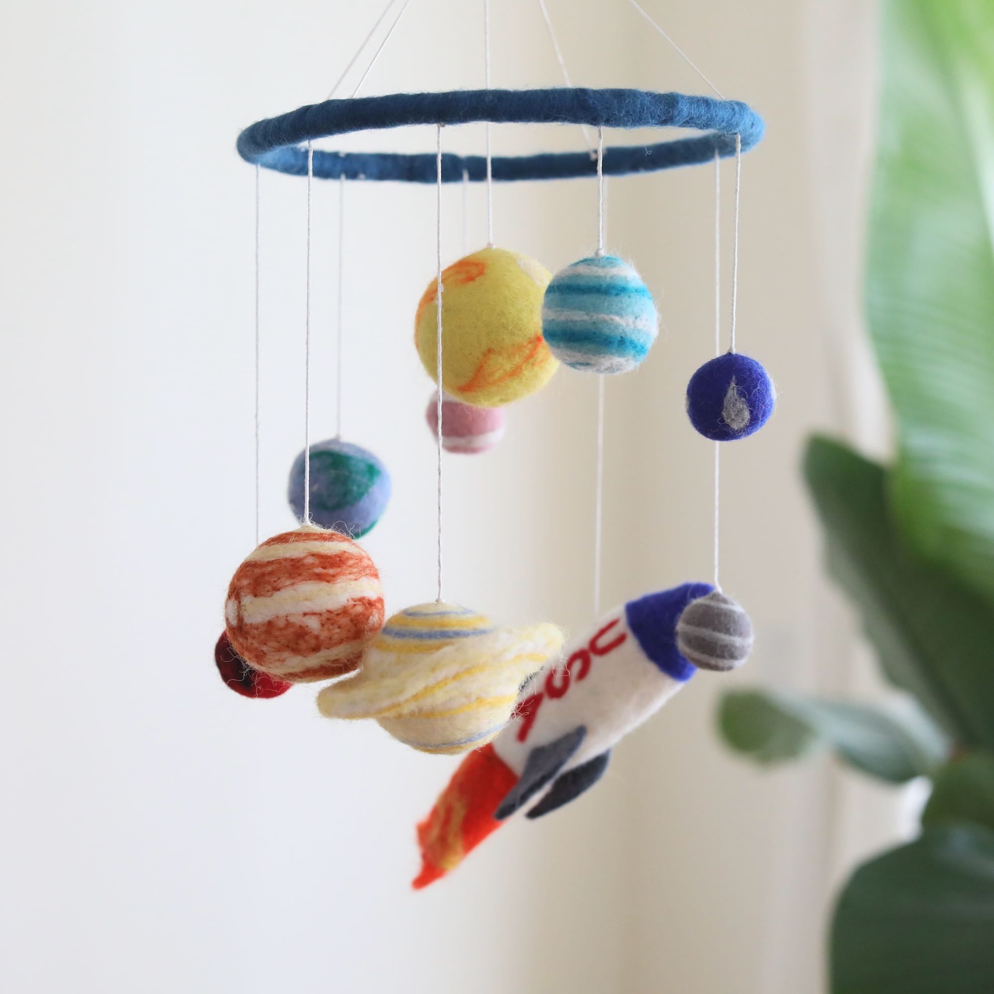 Mobile - Felt Baby - Solar System featuring soft felt planets and a rocket hanging from a blue ring, designed as a cozy baby accessory for imaginative play in a children’s boutique.