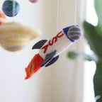 Close-up of a felt rocket ship with “USA” letters and flame details hanging in a Mobile - Felt Baby - Solar System, featuring soft, neutral tones for a stylish children’s boutique nursery.