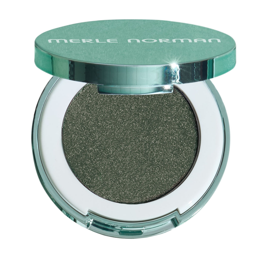 Merle Norman eyeshadow compact in a shimmering olive green shade, shown open with the metallic teal-green lid resting on top against a white background.