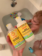 Hand holding California Baby - Calendula™ Shampoo + Conditioner Bundle near a toddler bathing in a tub with bath toys, highlighting gentle, soothing baby hair and body care essentials.